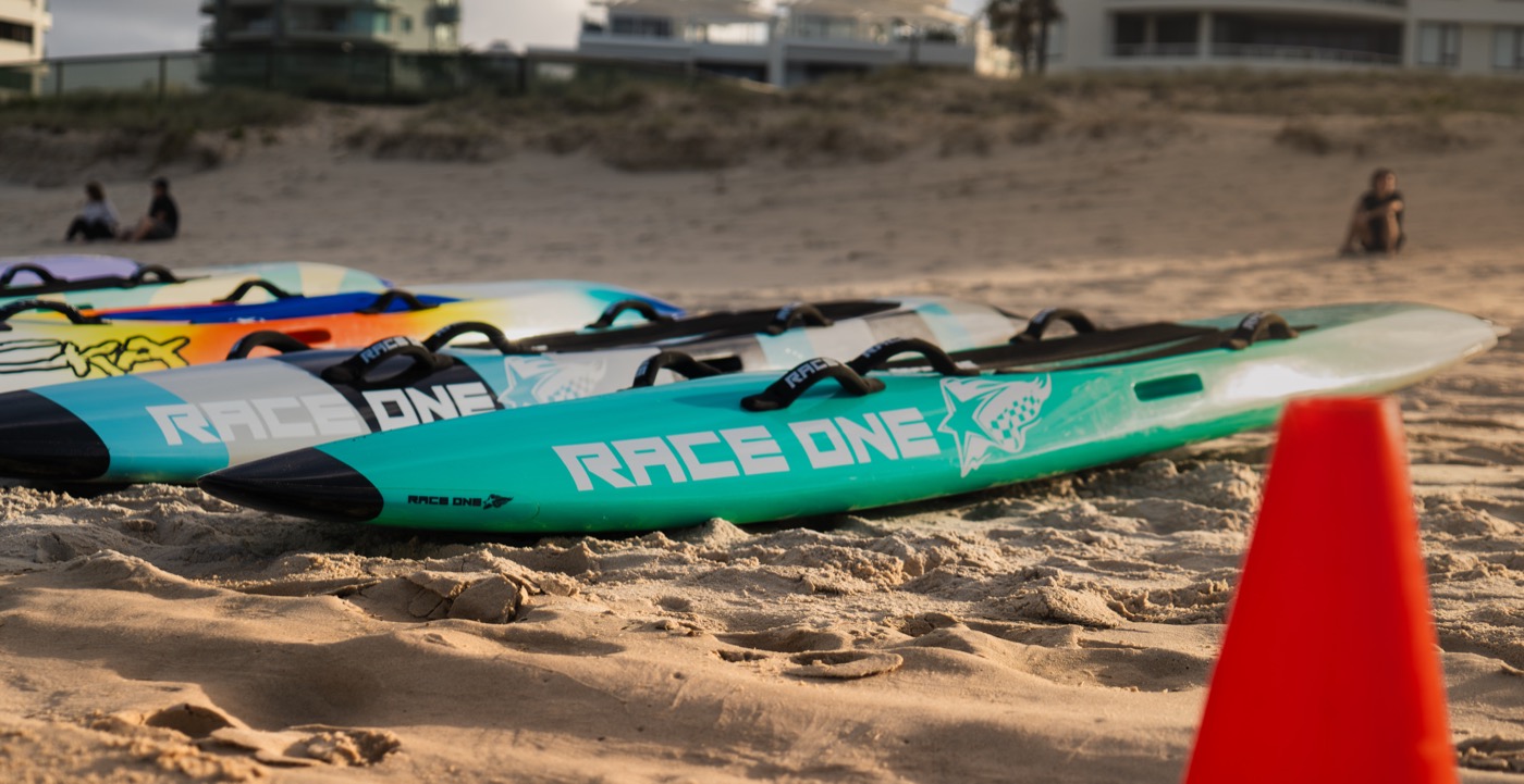 Race One paddleboards lined up on the sand at golden hour before a surf lifesaving carnival