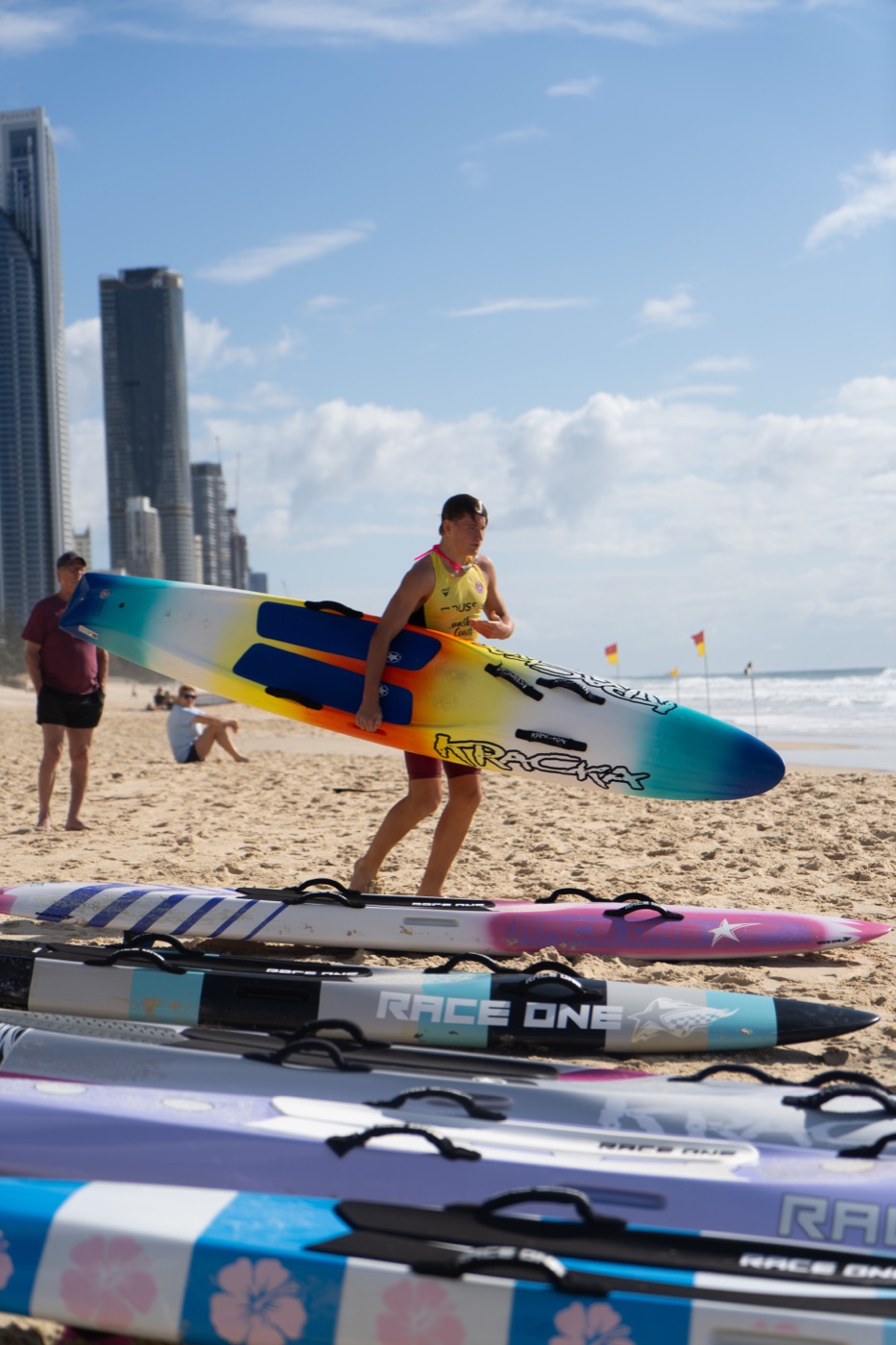 Young surf lifesaver carrying his racing board across the beach with the Surfers Paradise skyline behind