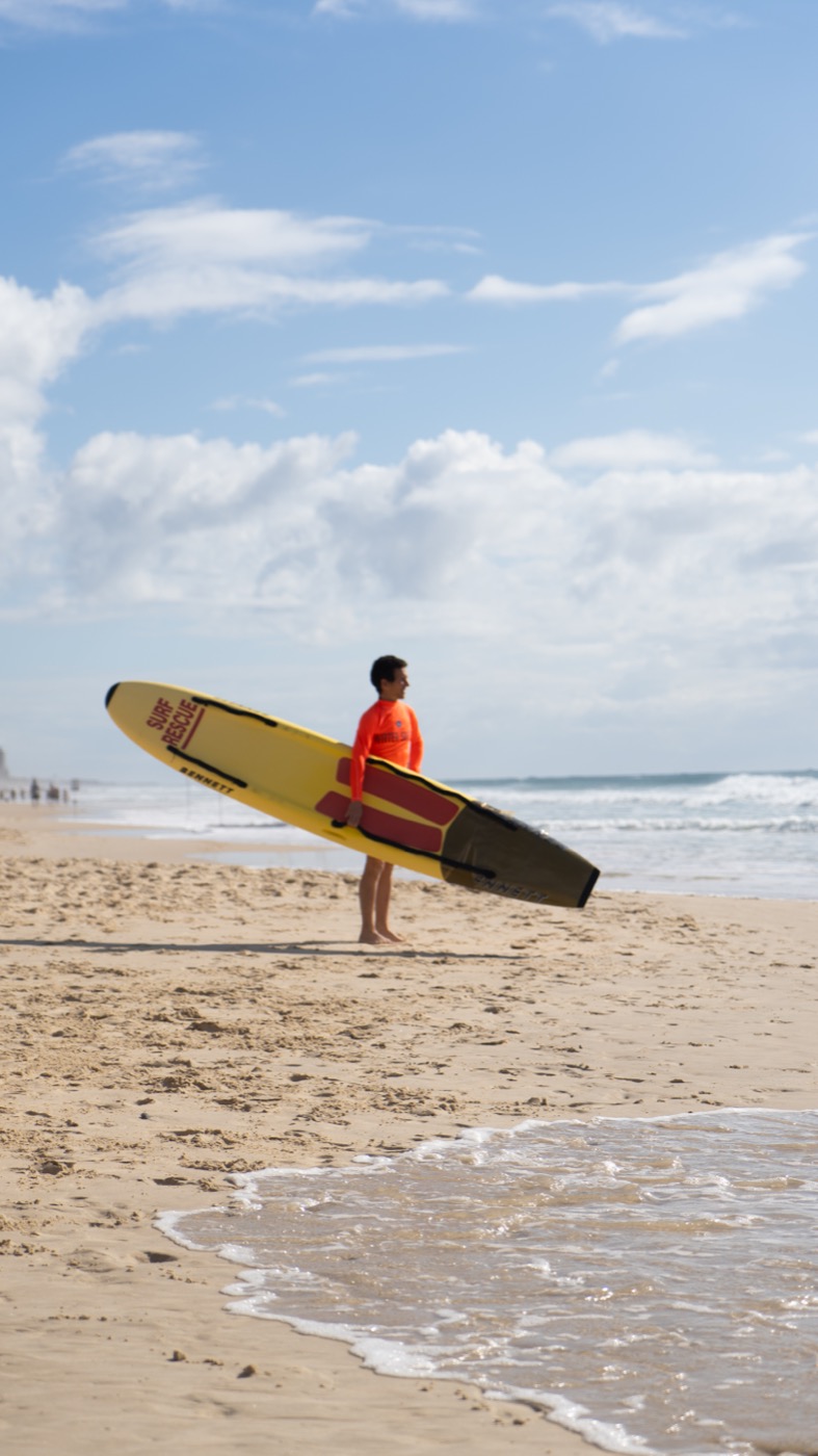 Lifeguard standing at the shoreline with a yellow surf rescue board